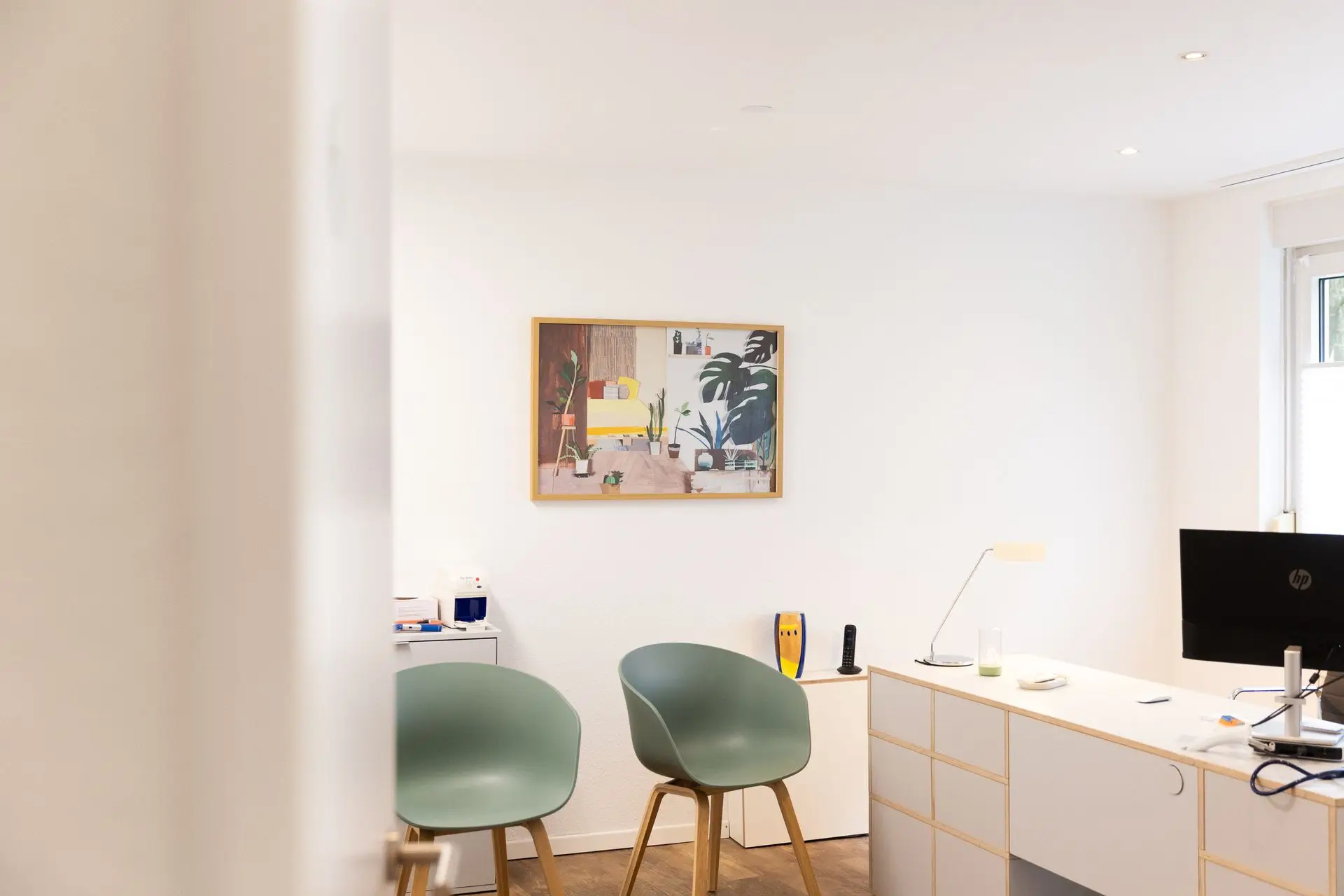 Helles Sprechzimmer mit zwei grünen Stühlen und Schreibtisch